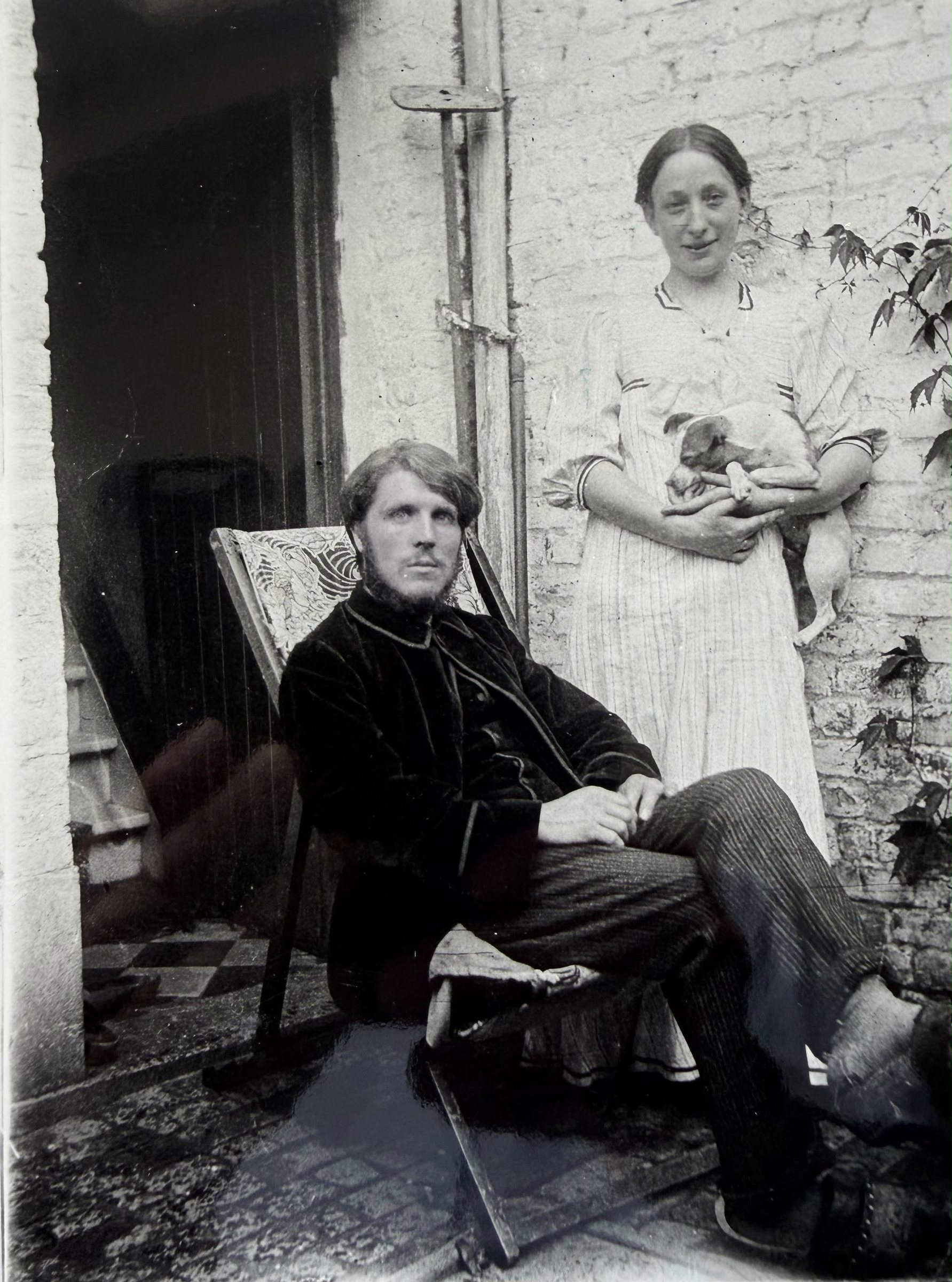 Rik Wouters seated in a deckchair with Nel standing behind him holding a puppy