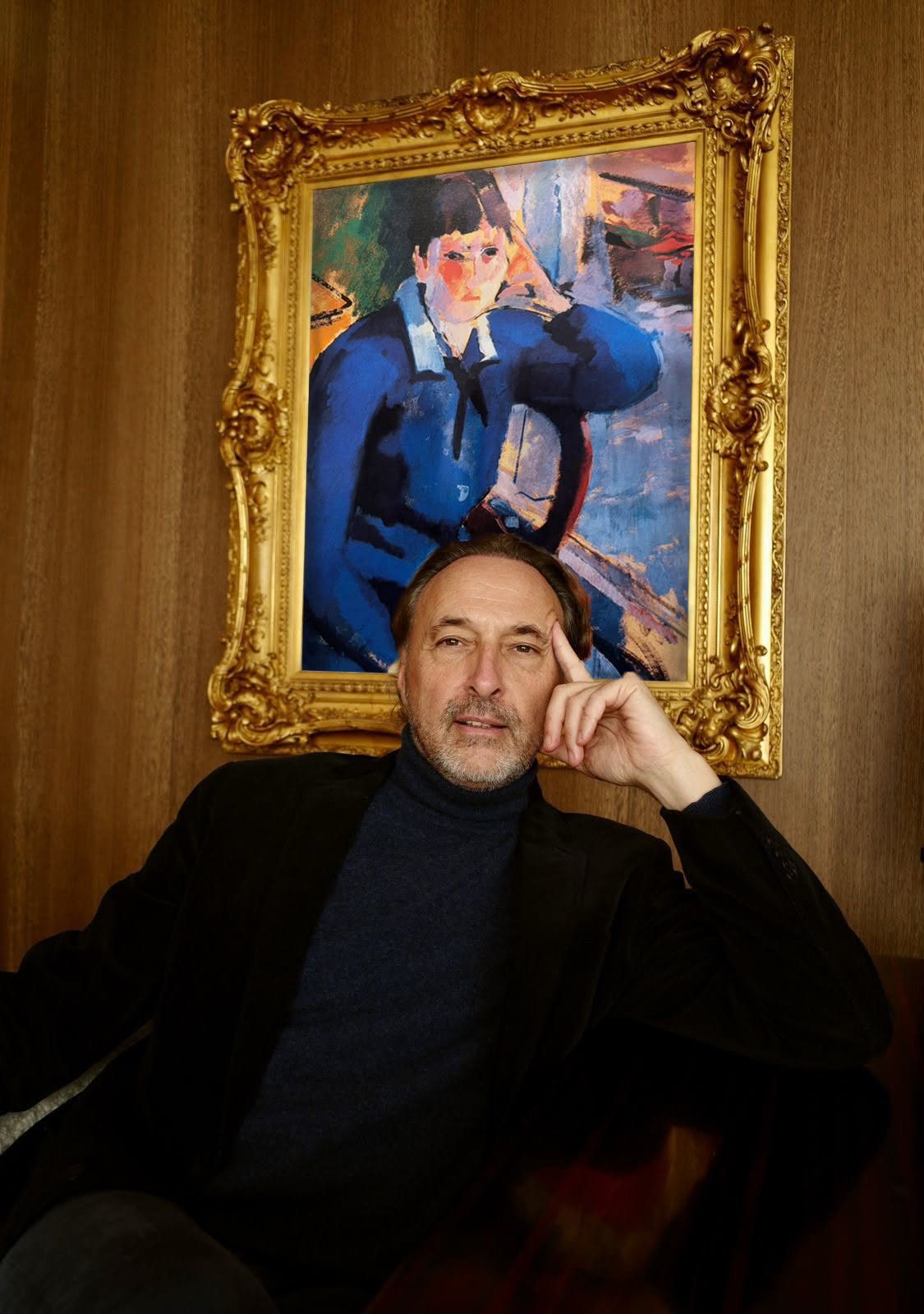 Olivier Bertrand seated in a dark jacket beneath a gilt-framed painting