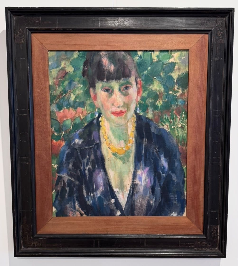 Portrait of a woman with a fringe and a yellow bead necklace against green foliage